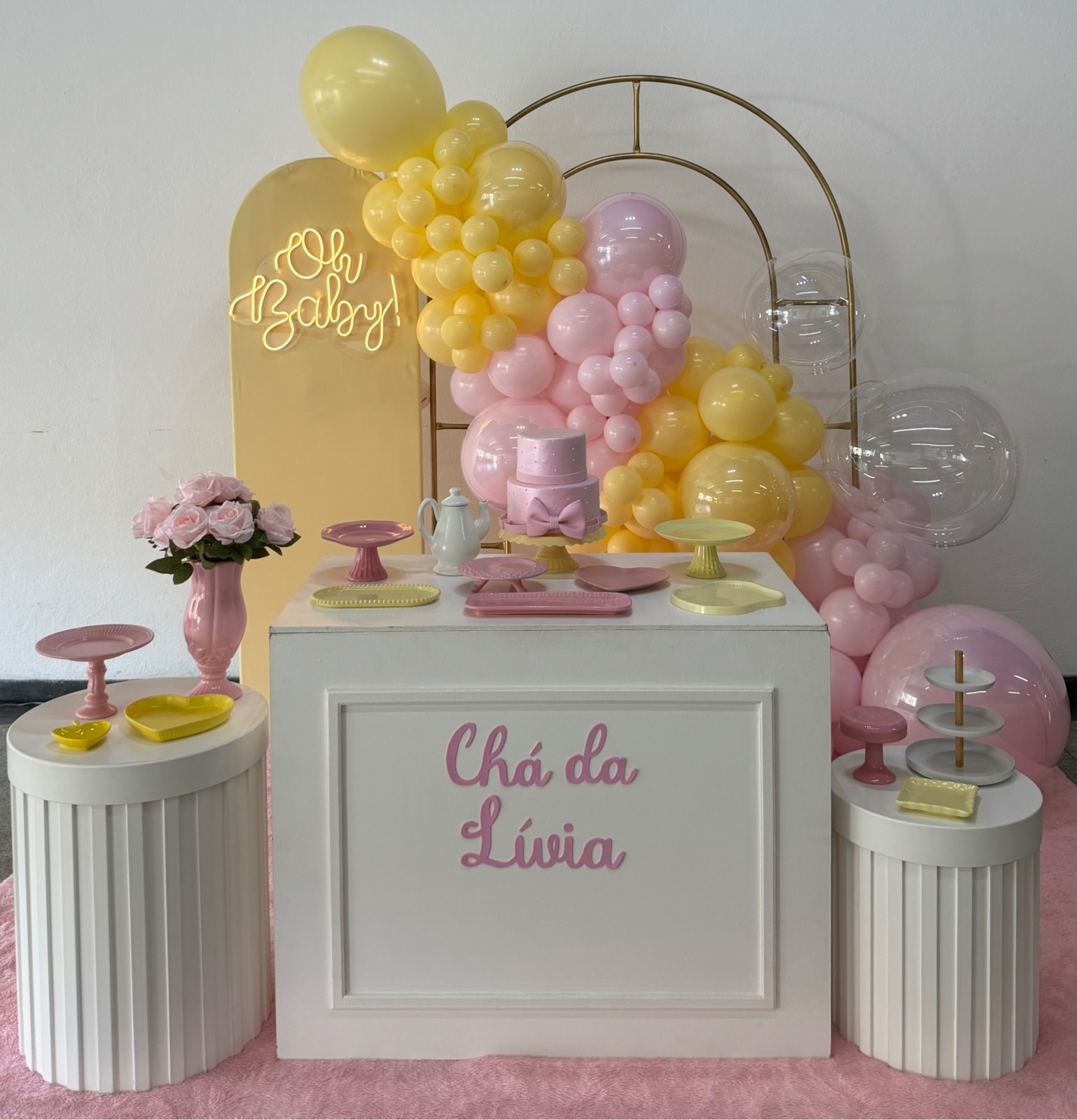 Decoração de chá de bebê com balões rosa e amarelo, painel dourado e mesas brancas